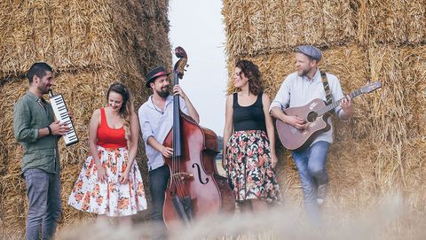 Cologne musicians stand in front of a straw wall with their instruments.