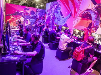 Leute sitzen auf der gamescom nebeneinander an Bildschirmen und spielen Videospiele
