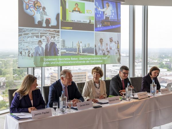 The management of Koelnmesse and Cologne's mayor Henriette Reker sit in a row at the table for a financial press conference.