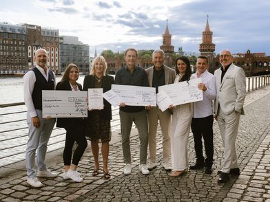 Several people are standing in a row along the Spree River, holding awards in their hands.